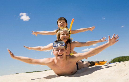 Portrait of cheerful couple and their son lying on sand and looking at camera